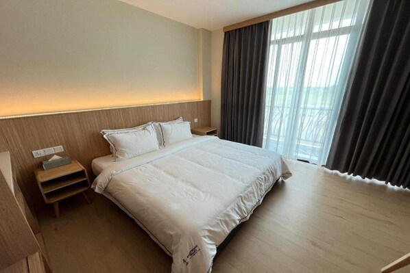 A hotel room with a large bed, a bedside table, a nightstand, and a window with curtains.