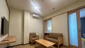 A room with a sofa, two chairs, a wooden table, a TV, and a sliding door. - Eastwood Valley Golf & Country Club (Miri)