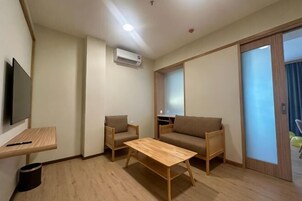 Una habitación con sofá, dos sillas, una mesa de madera, televisor y puerta corrediza.