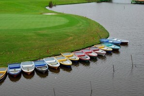 A row of small boats aligned along a water body adjacent to a green field.