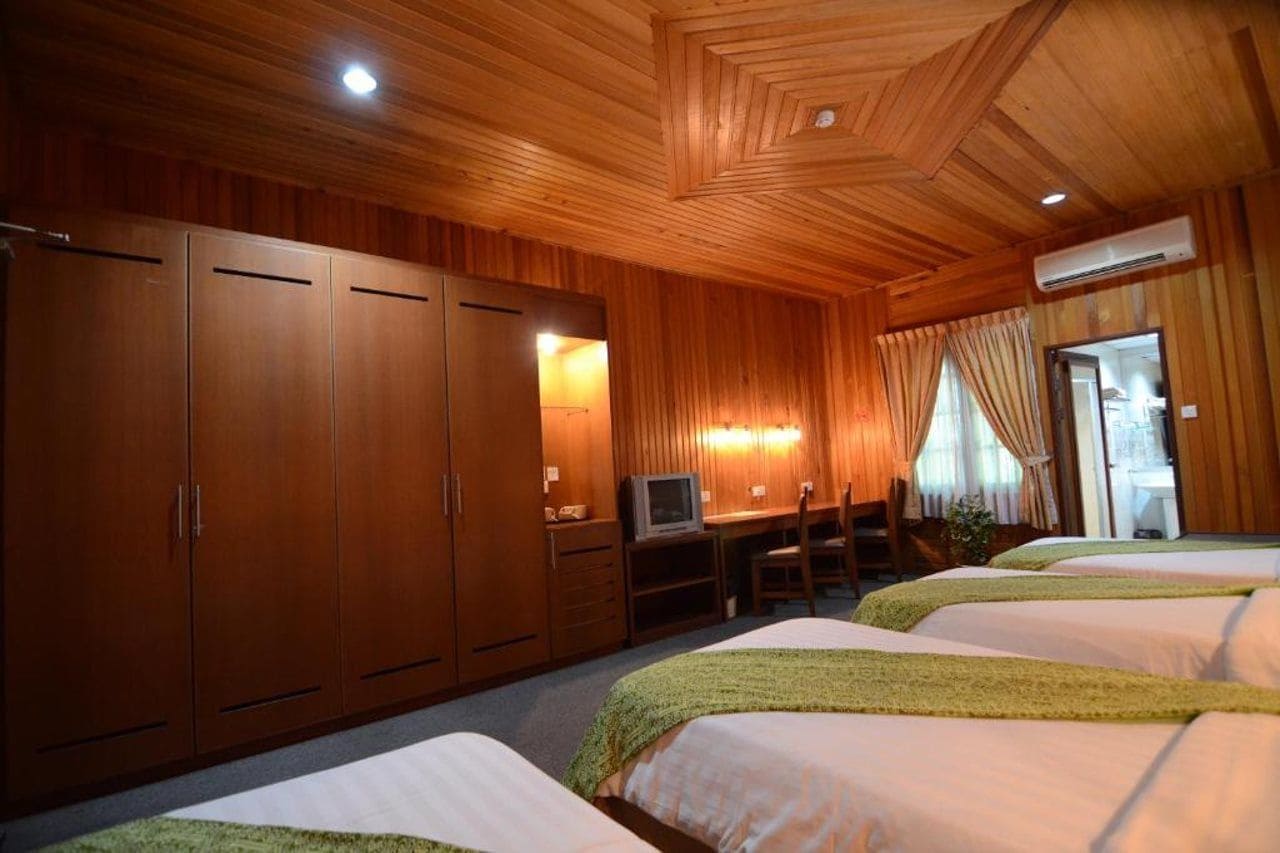 A hotel room with wooden paneling, a desk with a television, and two beds.
