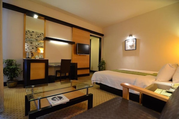 A hotel room with a bed, a desk with a chair, a television, and a mirror.