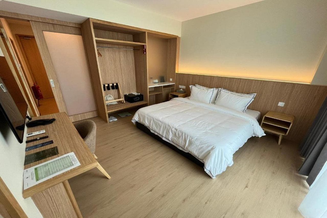 A hotel room with a bed, a desk, a wardrobe, and a bedside table.