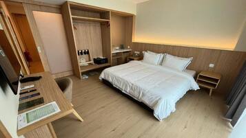 A hotel room with a bed, a desk, a wardrobe, and a bedside table.