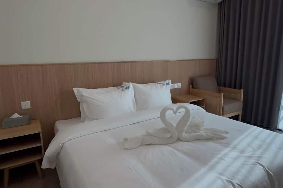 A hotel room with a neatly made bed, a wooden headboard, a bedside table with a tissue box, and a chair.