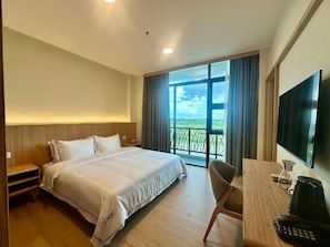 A hotel room with a bed, a desk with a telephone, a television, and a view of a balcony with a railing.
