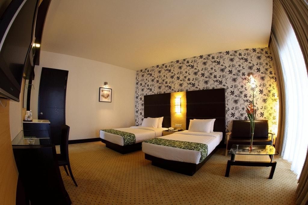 Ein Hotelzimmer mit zwei Betten, einem Schreibtisch, einem Sessel, einer Couch und einer dekorativen Vase.