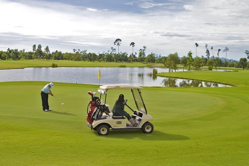 A golf course with a water hazard, a golf cart, and a golfer preparing to take a shot.