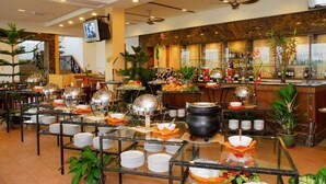 Disposição de buffet com várias estações de serviço, área de bar e uma tela de televisão na parede.
