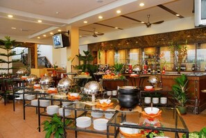 A buffet setup with multiple serving stations, a bar area with bottles, and a television mounted on the wall.