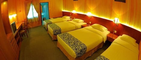 A hotel room with four beds, a desk, and a television.