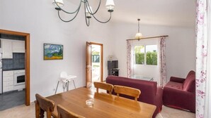 A dining area with a wooden table and chairs, a chandelier, a sofa, and a television. - Villas Geisan (Ciutadella de Menorca)