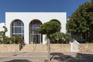 Um edifício moderno com três janelas em arco, uma escadaria de pedra e um passeio pavimentado.