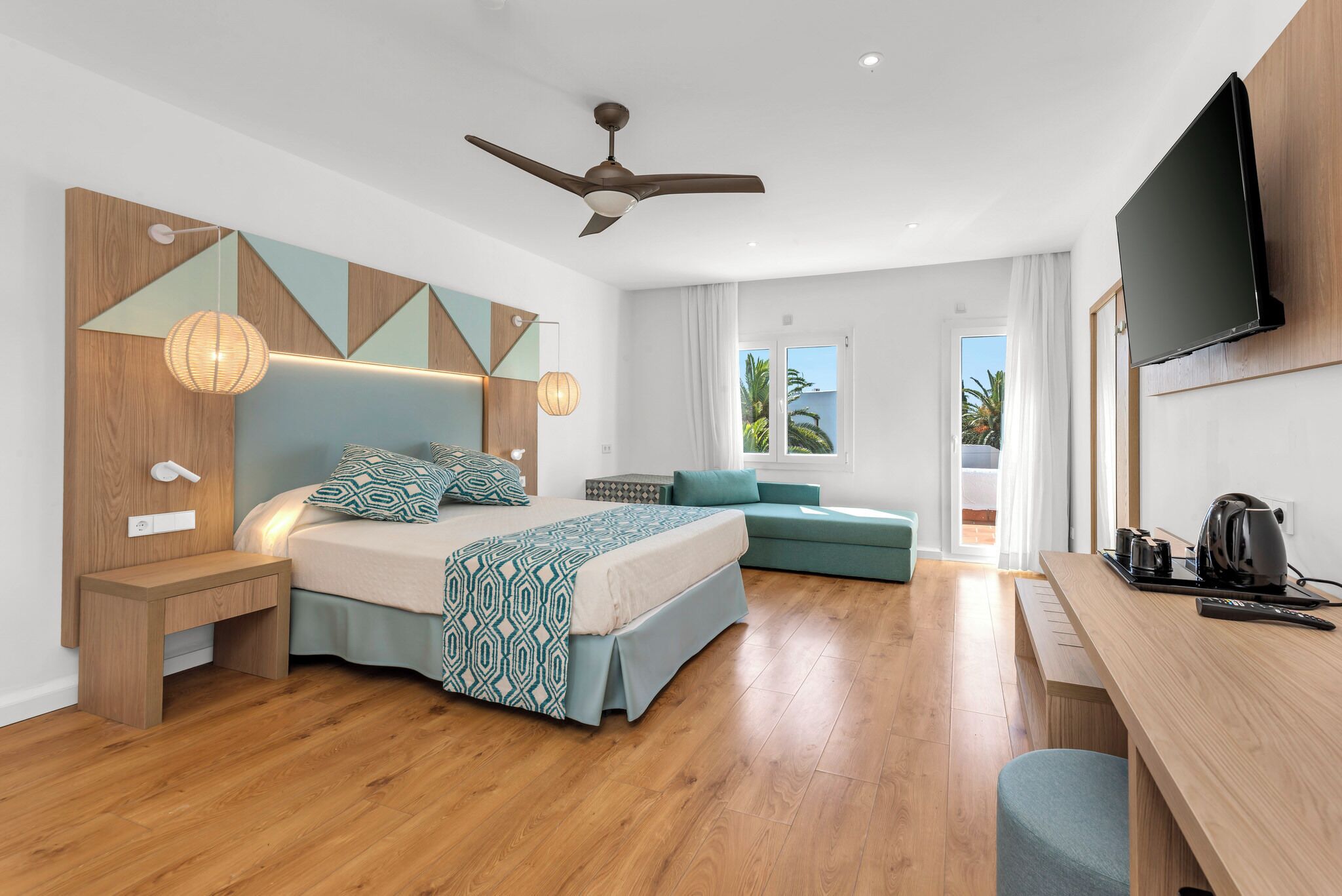 Una camera d'albergo moderna con un letto, una scrivania, una ventola a soffitto e una TV.
