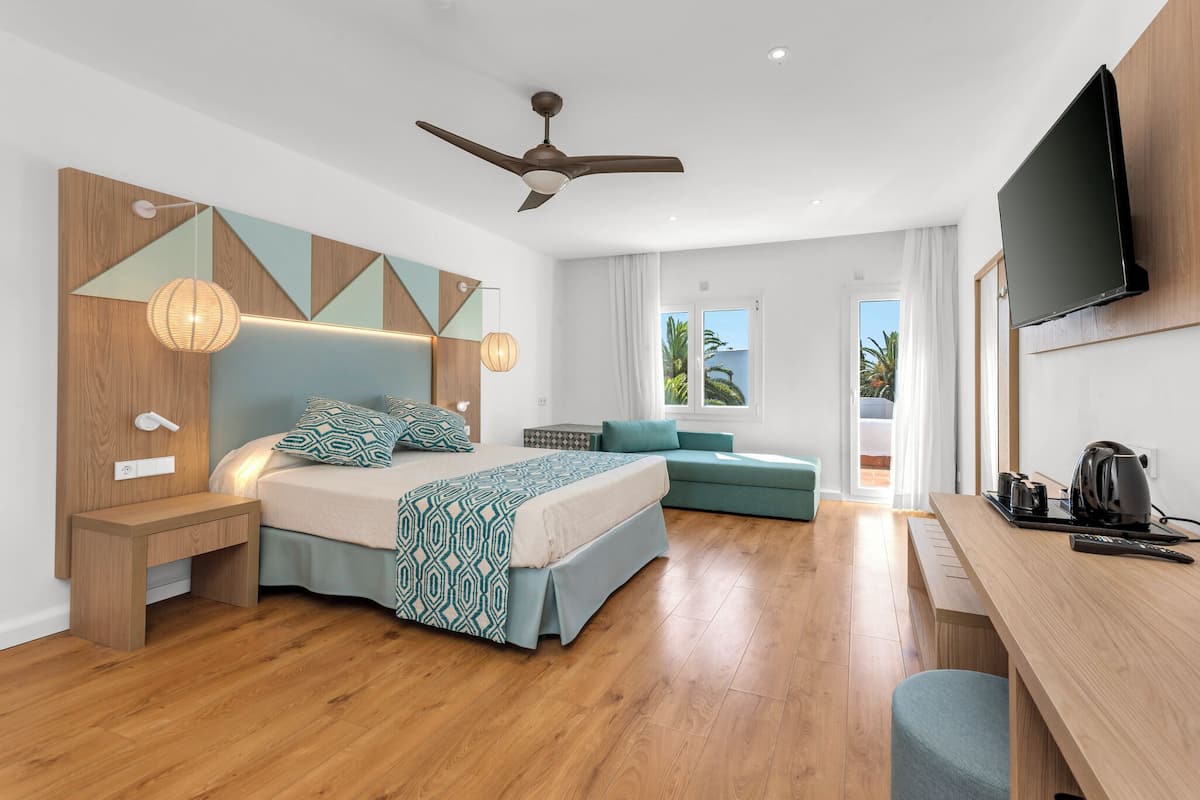 A modern hotel room with a bed, a desk, a ceiling fan, and a TV.
