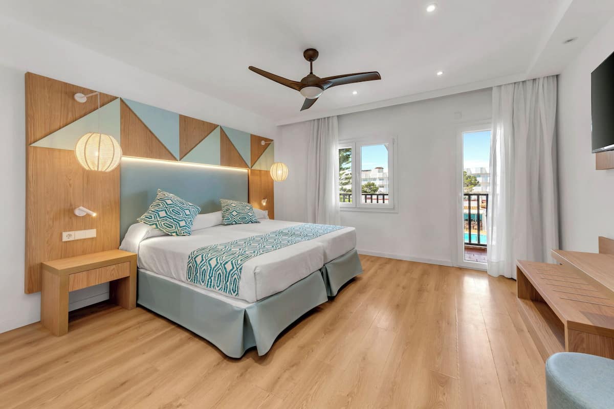 A modern bedroom with a bed, bedside tables, a ceiling fan, and a view of the outdoors.