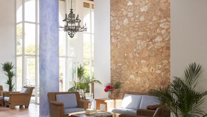 A spacious lobby with wicker furniture, a stone accent wall, and large windows allowing natural light. - Hotel Palia Dolce Farniente, (Santanyi)