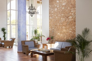 Un vestíbulo amplio con mobiliario de mimbre, un muro decorativo de piedra y grandes ventanales que dejan entrar la luz natural.