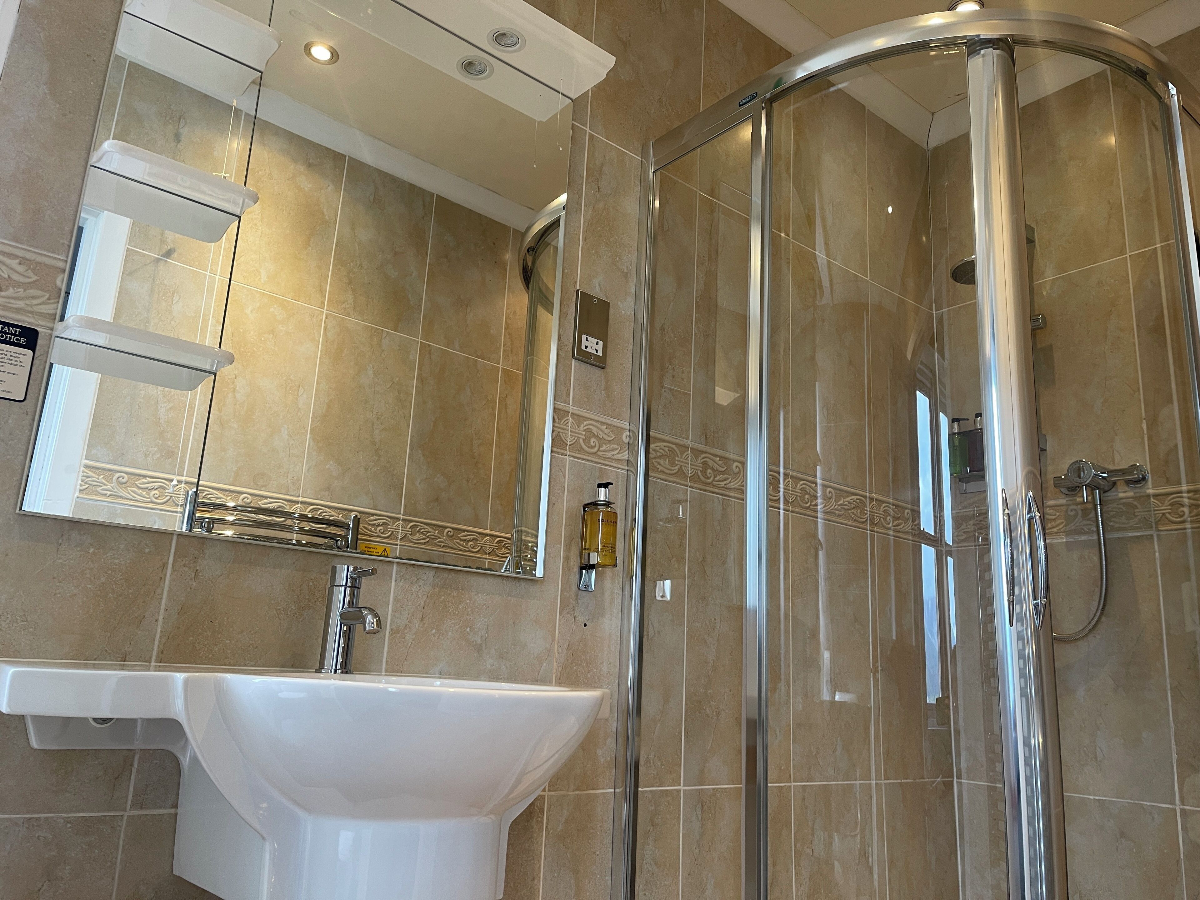 A modern bathroom with a glass-enclosed shower, a white sink, and a mirror with decorative tiles.