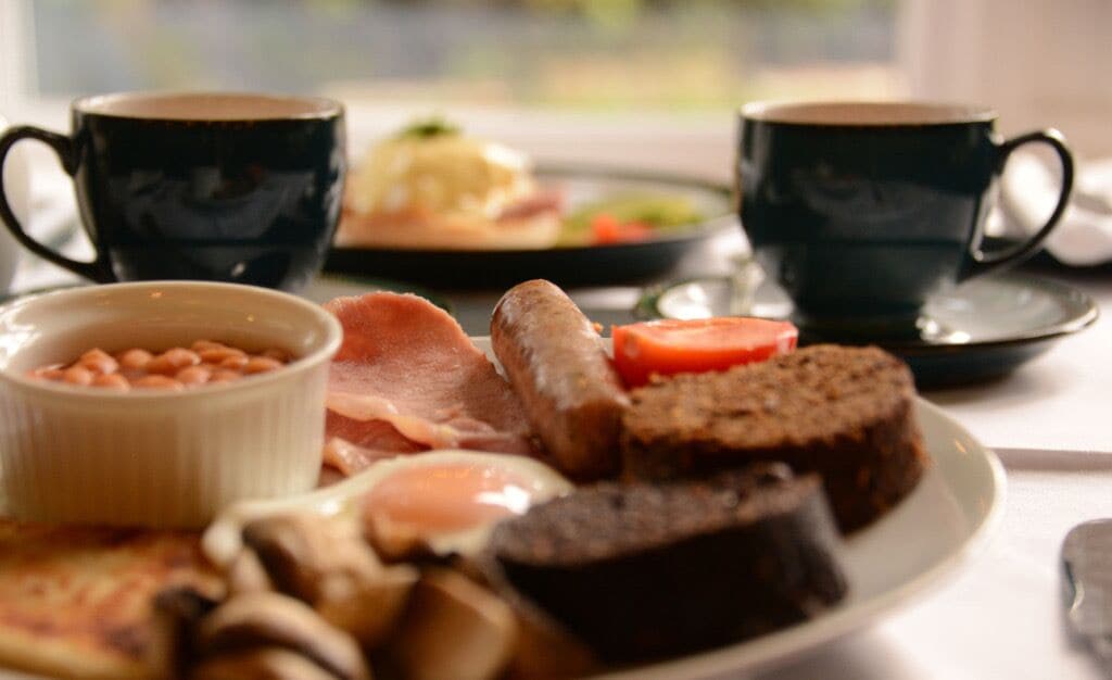 A breakfast plate with eggs, bacon, mushrooms, and toast, accompanied by two cups of coffee.