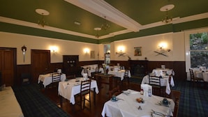 A dining area with multiple tables set for service, a fireplace, and wall-mounted light fixtures. - Creag Mhor Lodge (Fort William)