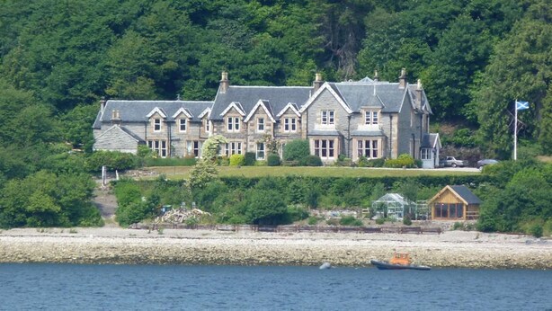 A large stone house with multiple gabled roofs, situated on a hillside with a view of the sea. - Creag Mhor Lodge (Fort William)