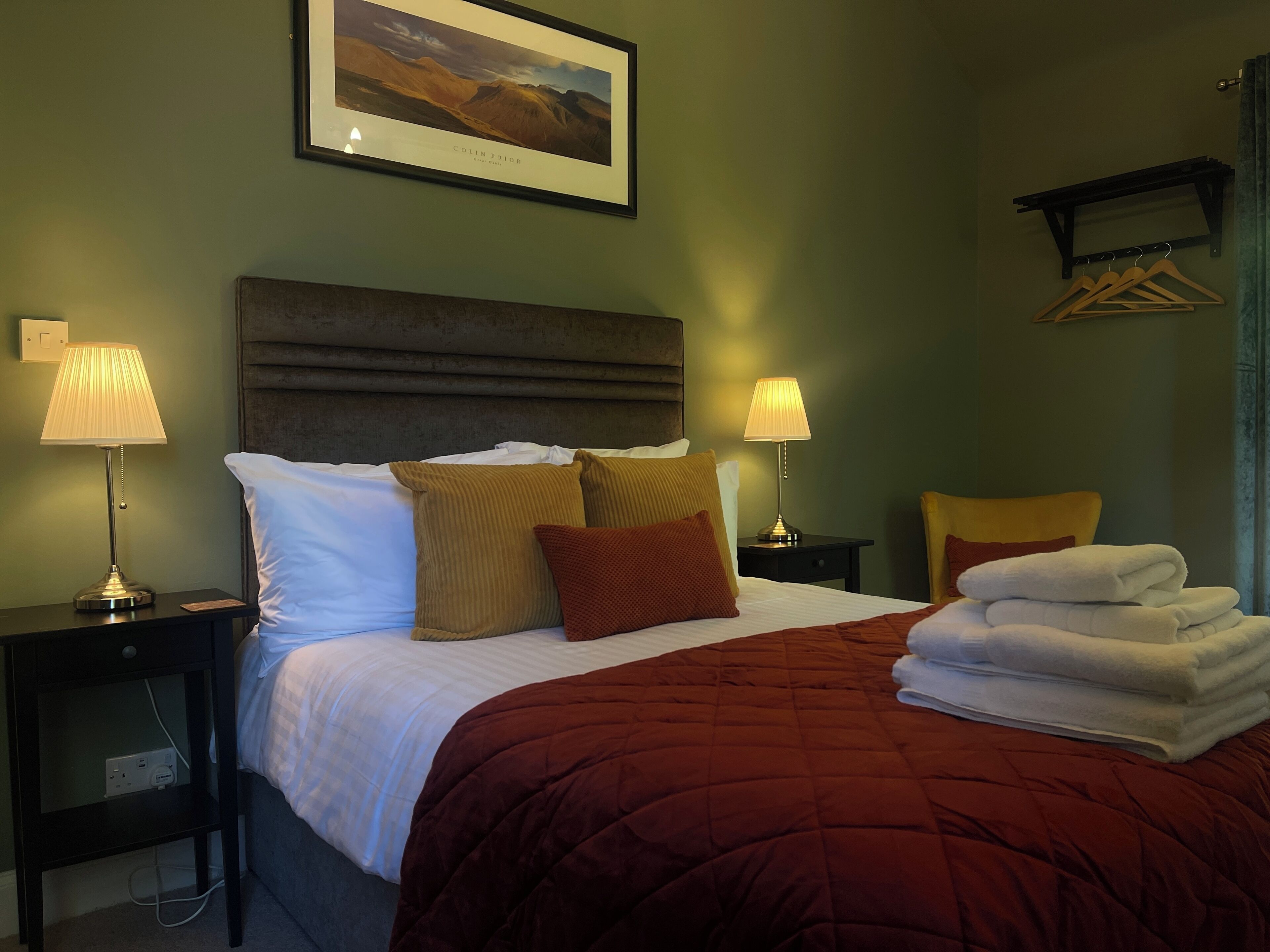 A hotel room with a large bed, two bedside tables with lamps, a headboard, and a framed picture on the wall.