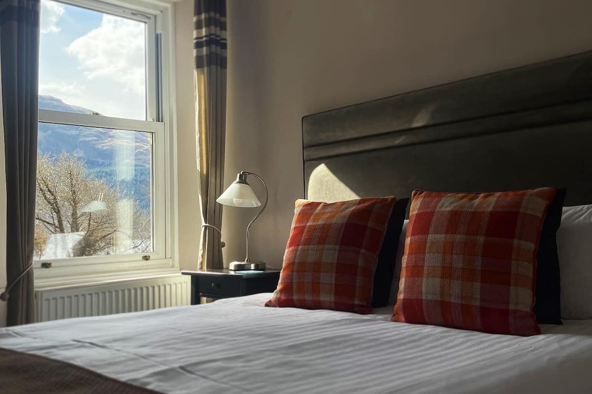 Une chambre d’hôtel avec un lit, une table de chevet, une lampe et une fenêtre avec des rideaux.