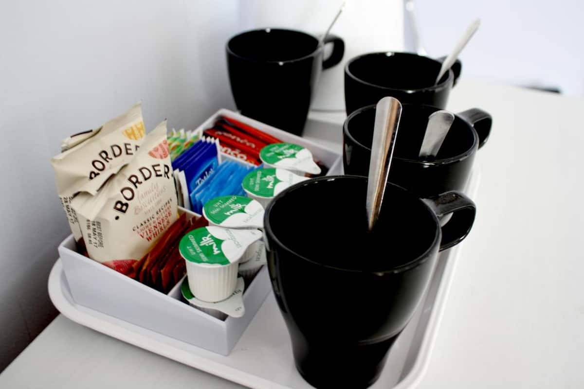 Un plateau avec des tasses noires et un paquet de café, ainsi que quelques aliments emballés.