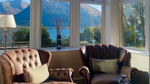 A room with two leather armchairs facing a large window overlooking a mountainous landscape. - Creag Mhor Lodge (Fort William)