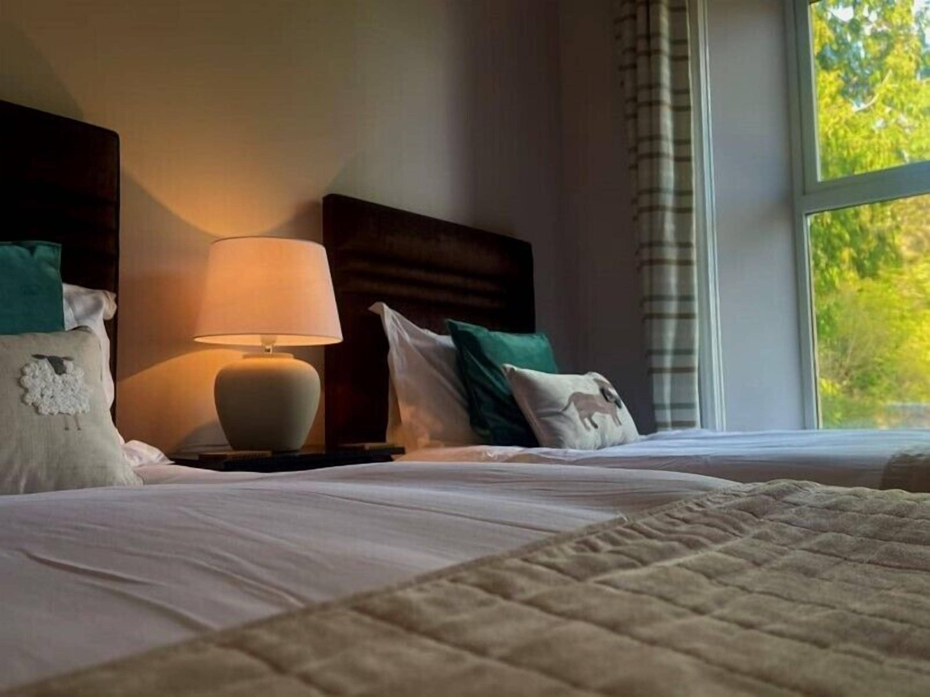 Un lit bien fait, avec une couette blanche et une couverture beige, une lampe de chevet et une tête de lit en bois foncé.