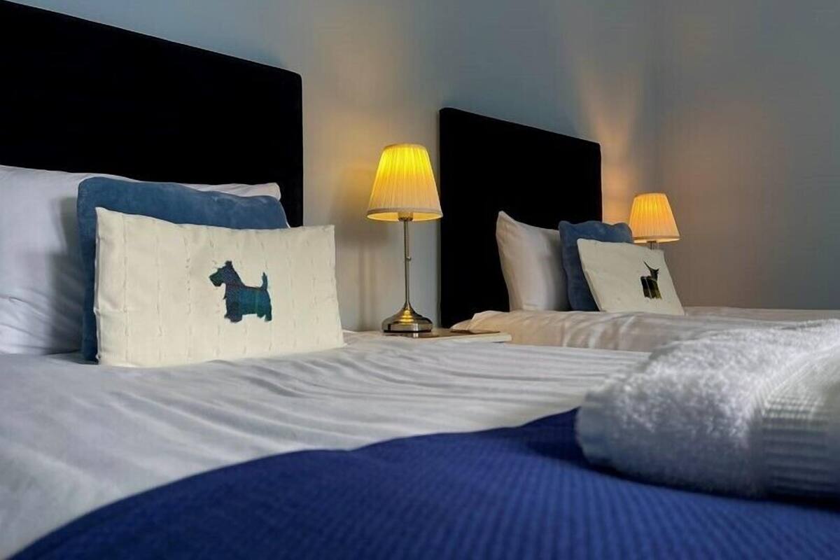 Une chambre d’hôtel avec deux lits, chacun doté d’une tête de lit, d’une lampe et d’un oreiller orné de la silhouette d’un chien.
