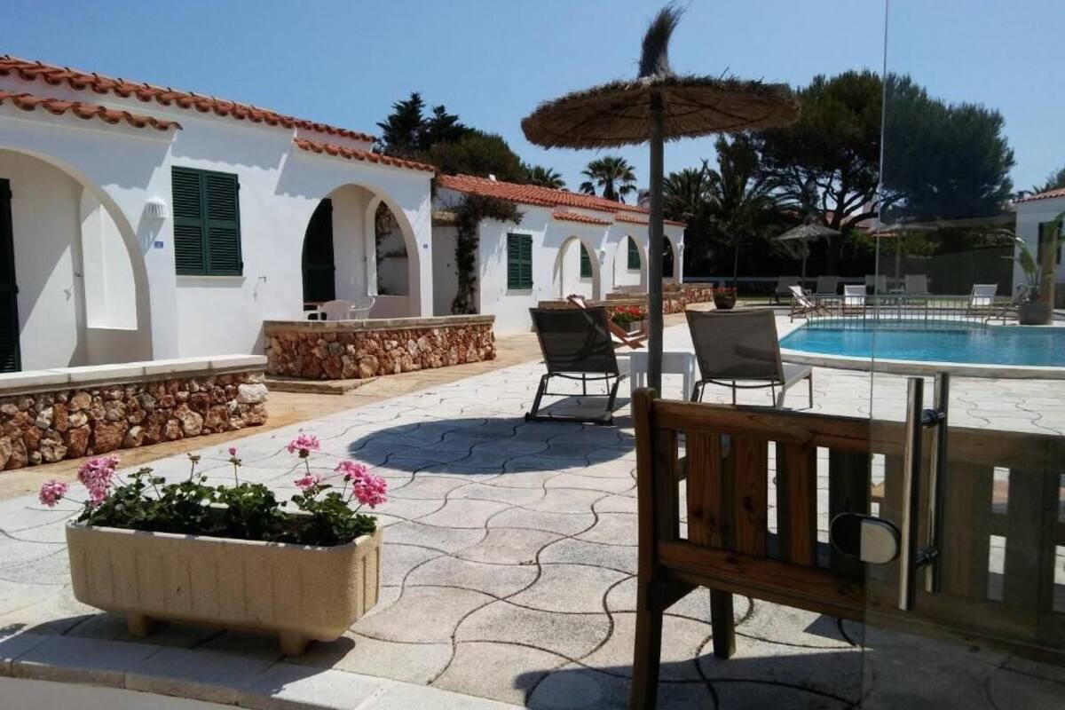 A poolside area with a bench, lounge chairs, and a thatched umbrella.