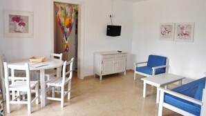 Un salon avec une table blanche, des chaises, un canapé bleu, un meuble blanc et un téléviseur fixé au mur.