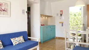 Une pièce avec un canapé bleu, un coin cuisine doté de meubles de couleur turquoise et une table à manger avec des chaises.