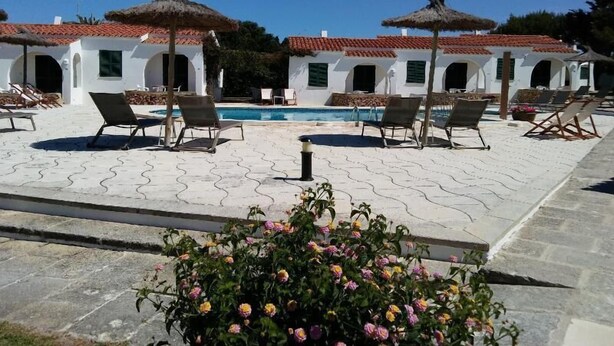 Un espace aménagé au bord de la piscine, avec des chaises longues et des parasols, une piscine et un bâtiment doté d’un toit recouvert de tuiles.