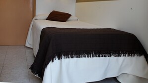 A single bed with a brown pillow and a black and white blanket. There is a wall-mounted light fixture above the bed. - Hotel Balear (Ciutadella de Menorca)