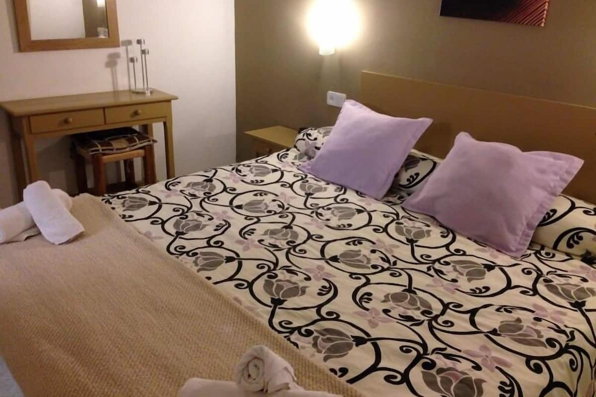 Una habitación de hotel con cama, mesita de noche, escritorio y espejo.