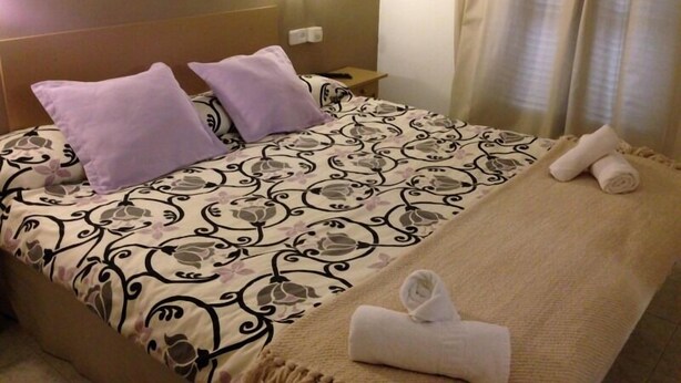 A hotel room with a bed, two pillows, a blanket, and a rolled towel on the bed. - Hotel Balear (Ciutadella de Menorca)