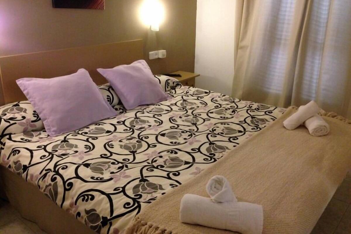 Una habitación de hotel con una cama, dos almohadas, una colcha y una toalla enrollada sobre la cama.