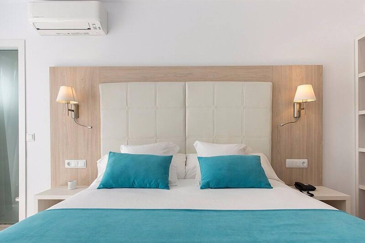 Une chambre d’hôtel avec un grand lit, deux tables de chevet, un climatiseur fixé au mur et deux lampes fixées au mur.