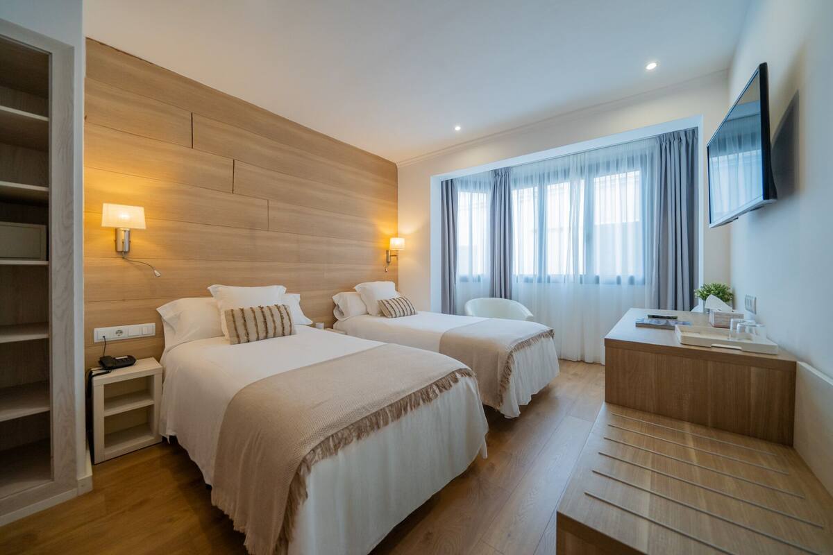 Une chambre d’hôtel avec deux lits, un bureau, une télévision et une fenêtre avec des rideaux.