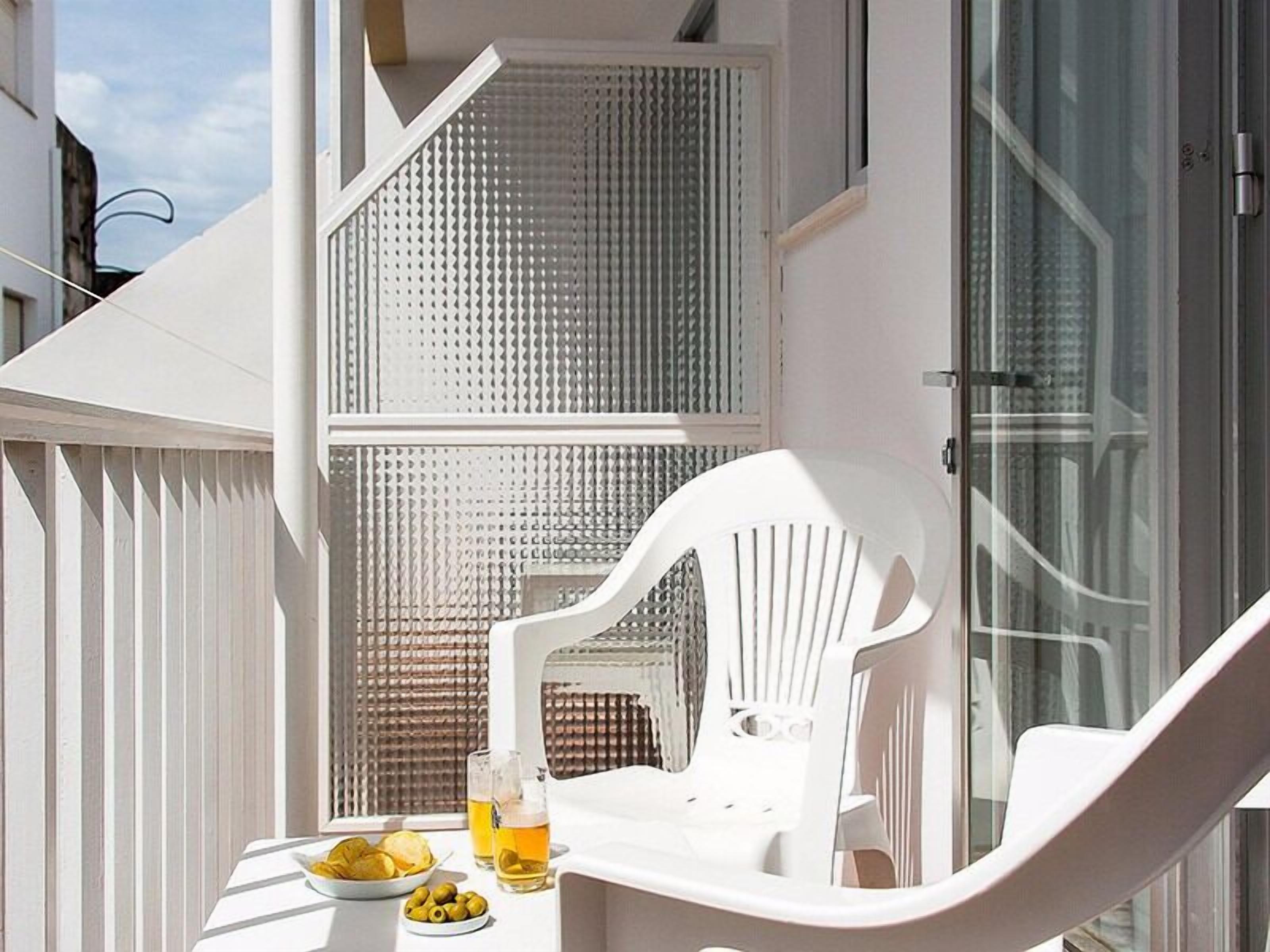 Un balcón con una mesa dispuesta para dos personas, una silla blanca y una cerveza en un vaso.