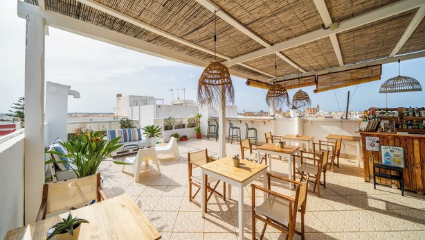 Un espace extérieur aménagé en terrasse, avec des tables et des chaises en bois, des lampes en osier suspendues et des plantes en pot.