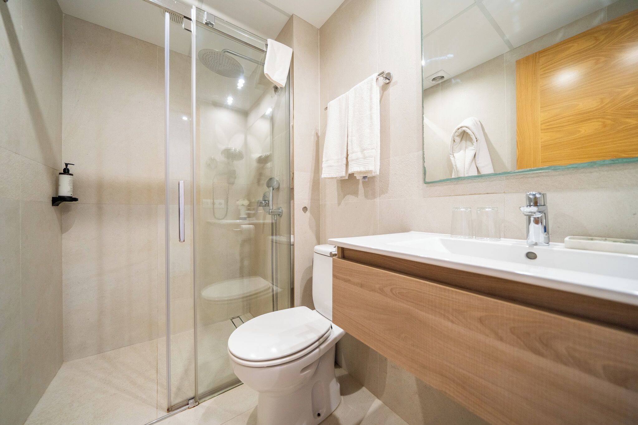 A modern bathroom with a glass shower enclosure, a white toilet, a wooden vanity with a sink, and a mirror above the vanity.