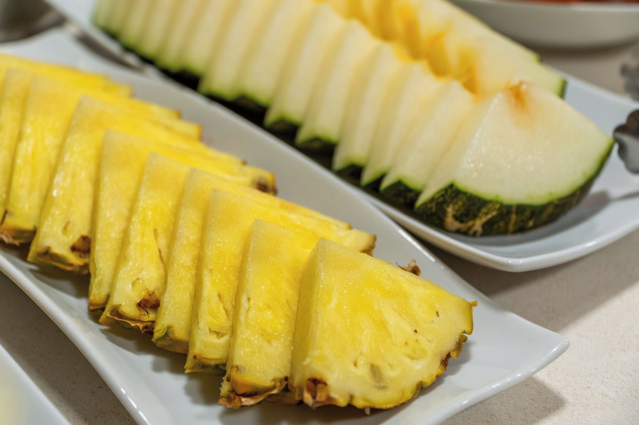 Valkoinen, suorakulmainen lautanen, jolla on siististi aseteltuja ananas- ja kesäkurpitsaviipaleita.