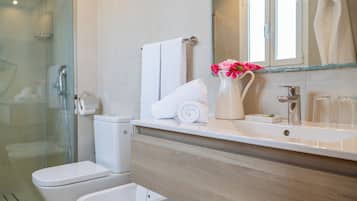 A modern bathroom with a glass shower enclosure, a toilet, a bidet, a sink with a mirror, and a vase with flowers.