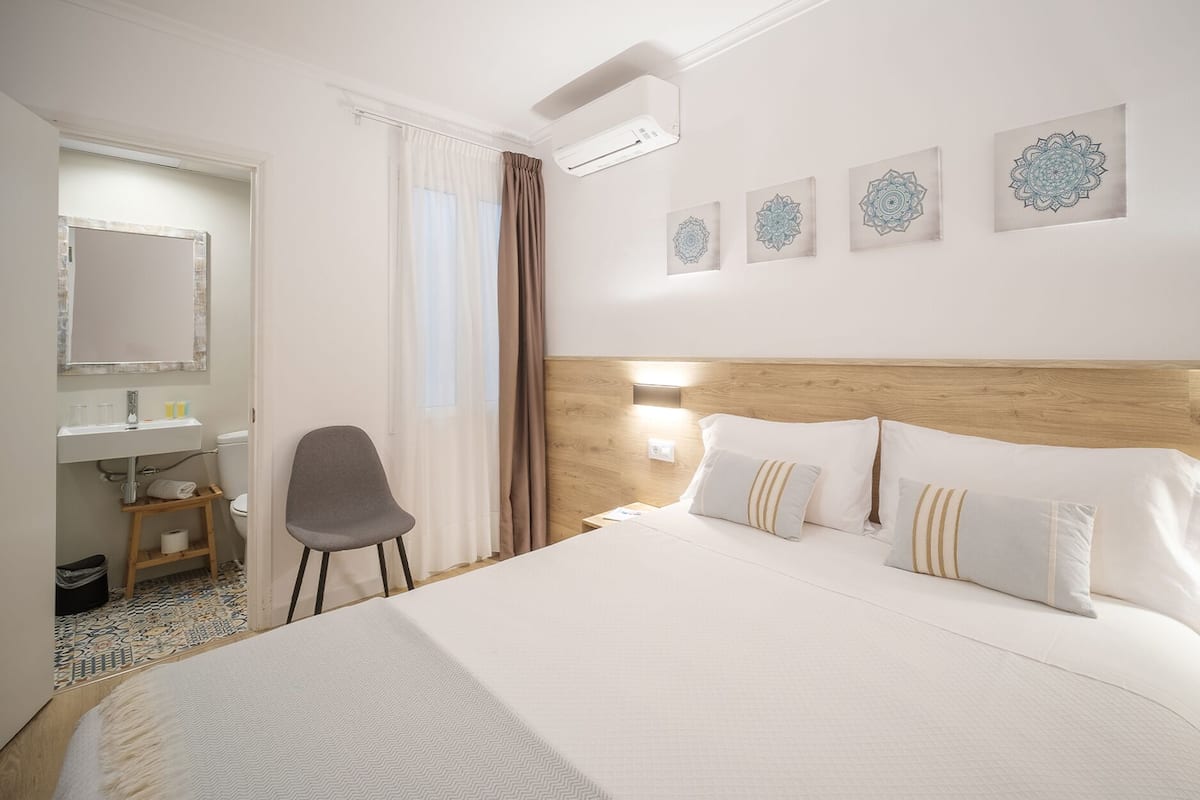 Une chambre d’hôtel comprenant un grand lit, une table de chevet, une chaise, une salle de bain avec un lavabo et des toilettes, ainsi que quatre éléments décoratifs fixés au mur.