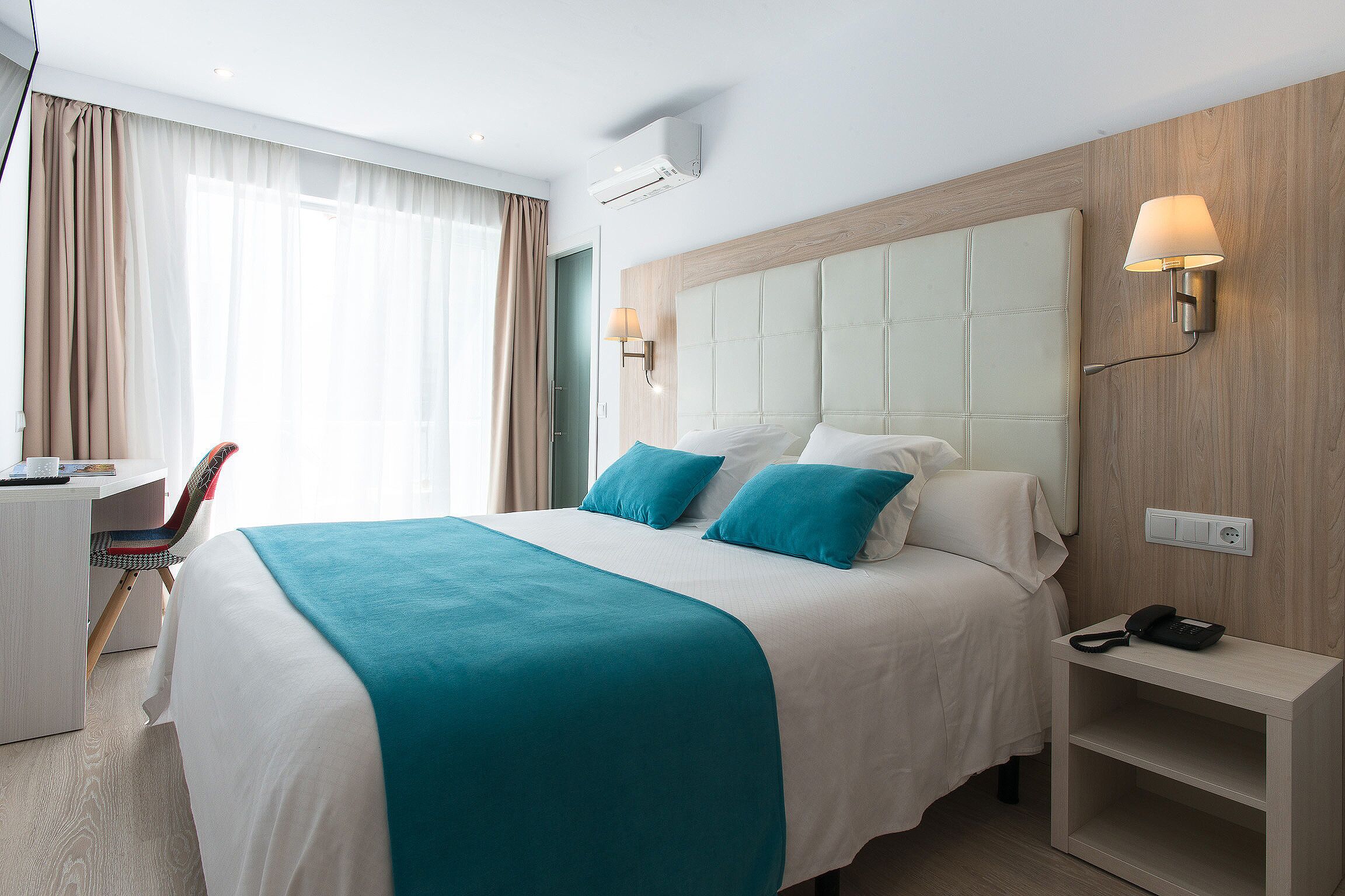 Ein Hotelzimmer mit Bett, Nachttisch und Schreibtisch mit Stuhl.
