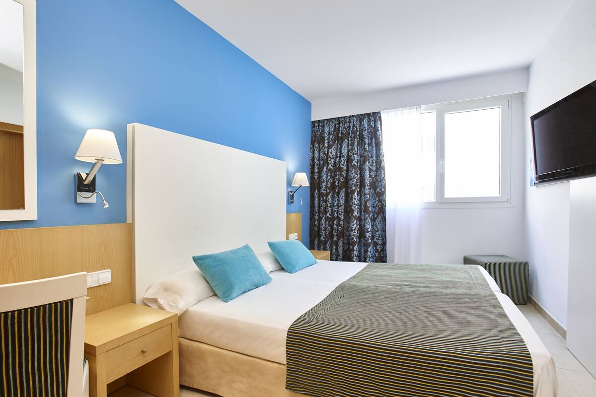 A hotel room with a bed, bedside tables, a TV, and a window with curtains.